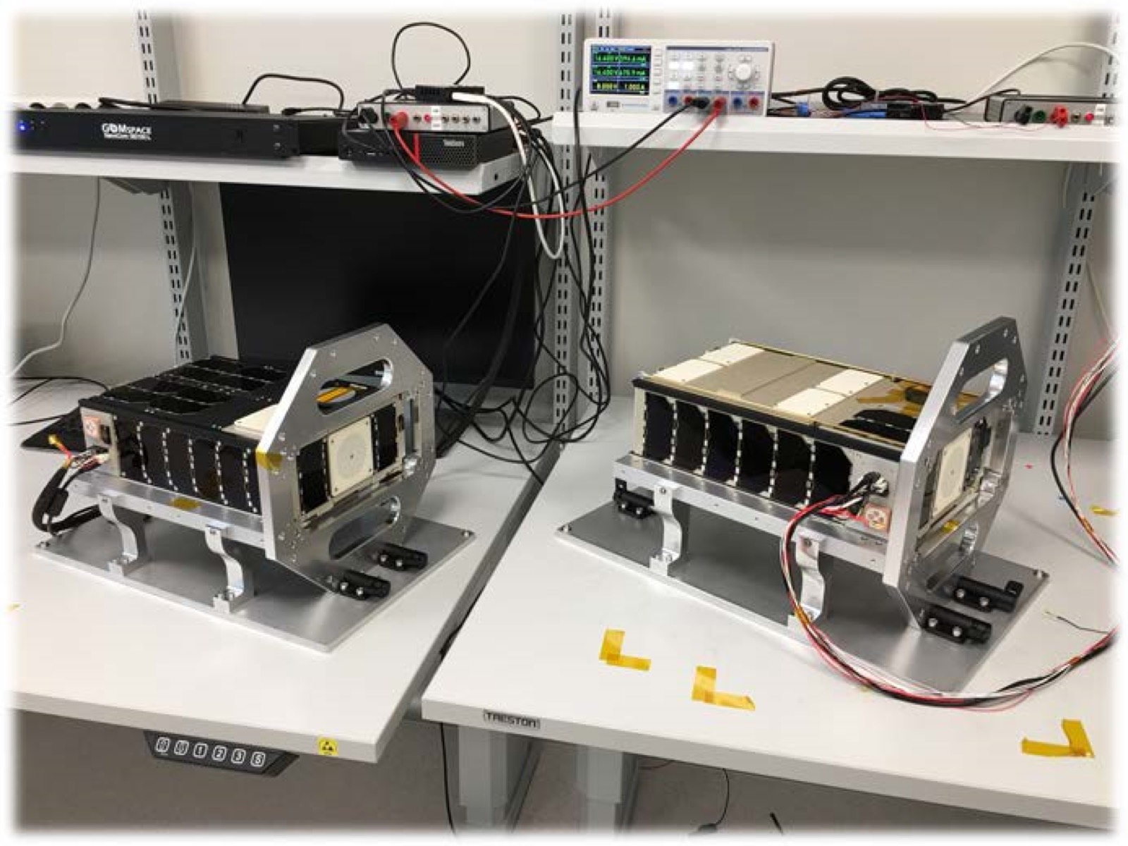 GOMX-4 flight models on the bench at GomSpace with ground-support electronics.